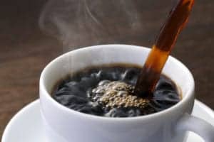 black coffee being poured into a white cup with a white saucer