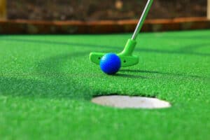blue miniature golf ball being putted in hole 