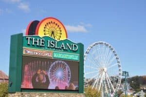 A large green sign for the Island in Pigeon Forge at day with the wheel in the background